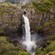 A large waterfall pouring through a rock face onto a valley below